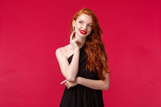 Fashion, luxury and beauty concept. Portait of elegant thoughtful and stylish redhead woman wearing black dress, evening makeup, touching earring, look up dreamy, imaging something, have idea.