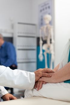 Close up of doctor supporting retired woman with physical pain, holding hands of patient to assure recovery and remedy. Medic comforting aged person with arthritis at physiotherapy