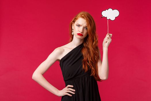 Portrait of sad and gloomy caucasian woman with red ginger hair, grimacing upset, feel down as have no ideas, hold cloud cardboard as if pondering, cant make up plan, red background.