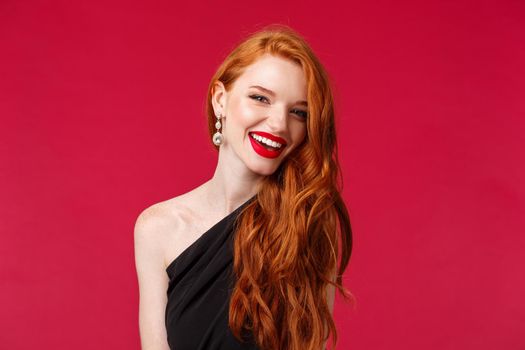 Close-up portrait of stylish successful and rich gorgeous redhead woman in luxurious black dress earrings, laughing and smiling at camera happy, attend evening charity event, red background.