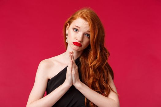 Close-up portrait of gloomy clingy attractive redhead girlfriend in black background asking for something, say please with cute silly face, pouting begging for help, hands pressed together in pray.