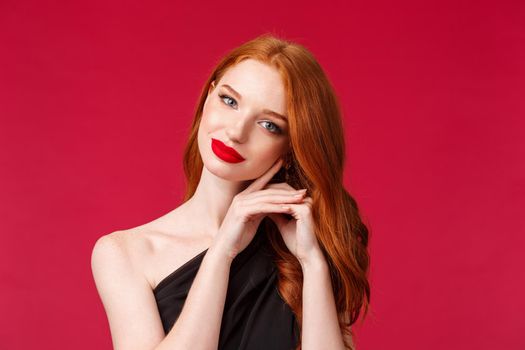 Close-up portrait of gorgeous feminine woman apply makeup, red lipstick, evening dress, look tender and seductive, tilt head coquettish and gazing camera, standing red background.