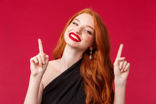 Elegance, beauty and fashion concept. Close-up portrait of fabulous carefree, happy smiling redhead woman feel like number one, having fun at party, enjoying and dancing, red background.