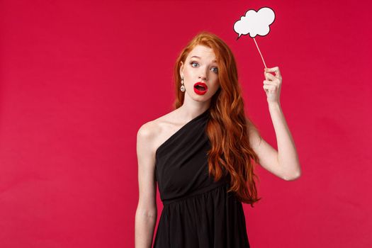 Portrait of clueless and indecisive attractive feminine redhead woman in black dress, holding cloud comment card over head as if dont have any ideas, cant think-up plan look gloomy, red background.