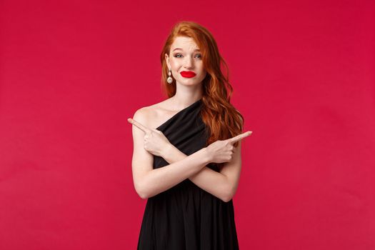 Fashion, luxury and beauty concept. Redhead woman troubled with decision, asking your opinion on two variants, grimacing unsure and indecisive, pointing sideways left right, wear black dress.