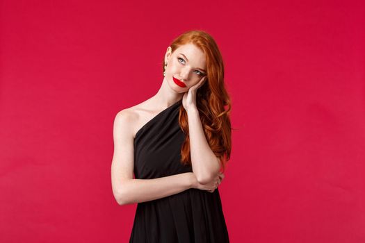 Waist-up portrait of annoyed and bored, bothered redhead woman in elegant black dress, sighing displeased, getting pressured, look up troubled and upset, stand red background.