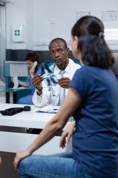 African american pediatrician doctor disucssing medical treatment with patient mother analyzing lungs radiography explaining xray expertise during appointment in hospital office. Health care service