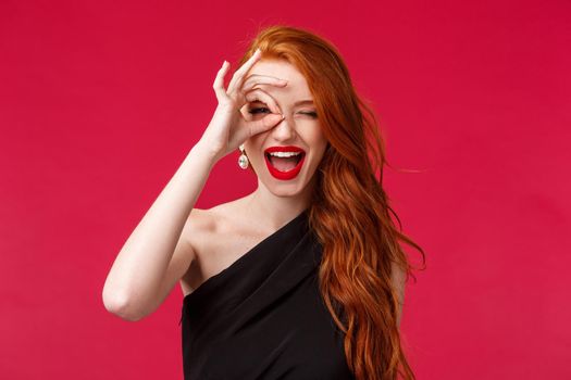 Close-up portrait of happy and excited good-looking redhead girl telling to grab your chance, show peace sign on eye and look through fingers as if seeing something on distance, smile pleased.