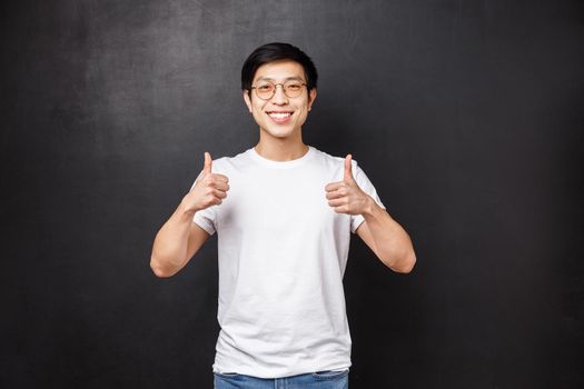 Cheerful good-looking asian young man in sunglasses in white t-shirt, show thumbs-up in approval, guarantee you will like, agree or accept something awesome, smile camera pleased.