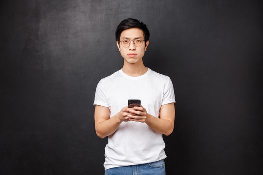 Technology, gadgets and people concept. Serious suspicious and dubious young asian guy dont believe person online telling truth, receive strange messge, squint camera uncertain, hold smartphone.