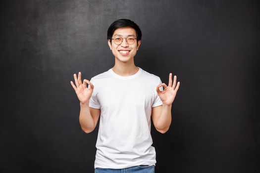 Everything be good, I guarantee. Relaxed happy smiling young asian man showing okay signs as assure all done great, work went well, rating excellent product, guarantee quality.