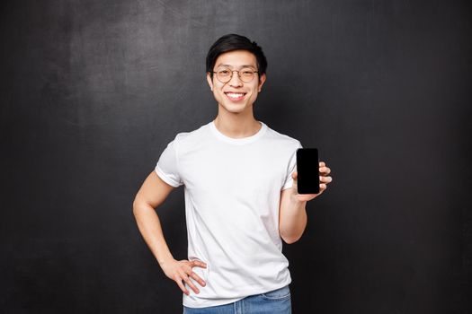 Technology, gadgets and people concept. Portrait of young male store clerk showing new features of smartphone, holding mobile phone and introduce application or company banner on gadget display.