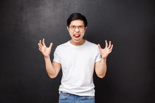Annoyed tensed, pissed-off asian man going insane from anger and hate, screaming aggressive gonna kill someone, clench raised hands into arms, grimacing hateful, standing black background.