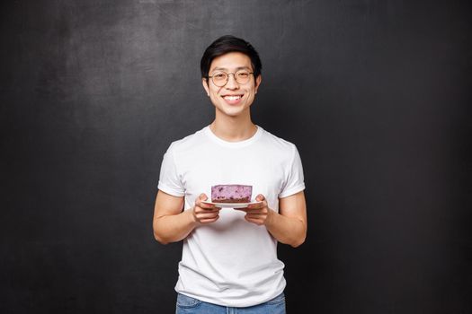 Portrait of cheerful caring handsome asian boyfriend bring piece of tasty cake for girlfriend, trying take care and do nice lovely gesture express sympathy, standing black background.
