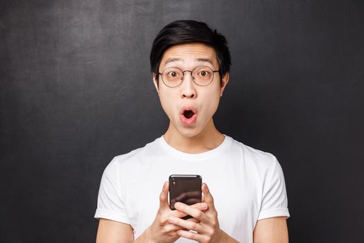 Technology, messaging and people concept. Close-up portrait of excited and amused happy asian man, smiling astonished and pleased, received positive reply in mobile phone messanger, hold mobile.
