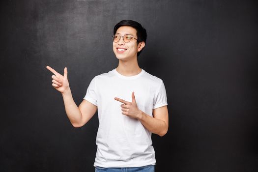 Handsome young healthy asian guy in white shirt contemplate something pleasant, smiling and looking upper left corner happy, see good offer, great opportunity, advertisement concept.