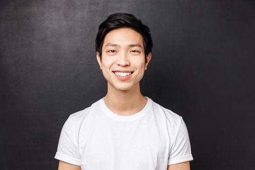 Close-up portrait of satisfied asian client smiling pleased, looking at camera, standing over black background with happy positive attitude, concept of emotions and people faces.