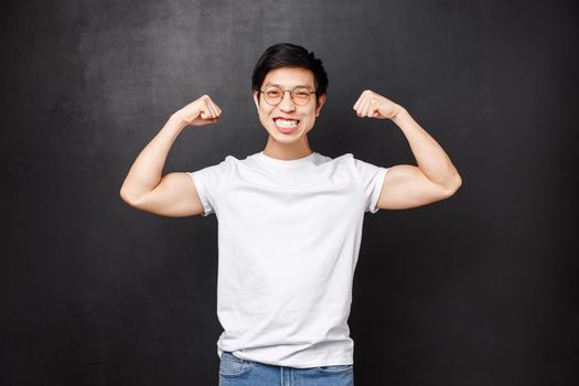 Sport, athletes and olimpics concept. Cheerful and strong young handsome boyfriend bragging with his strength, got fit for summer, flex biceps and smiling satisfied, black background.