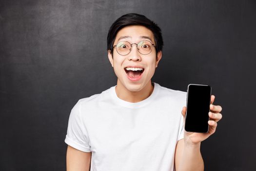 Technology, messaging and people concept. Close-up portrait of happy, surprised and impressed young excited asian man in white t-shirt, showing smartphone display amazed with cool app.