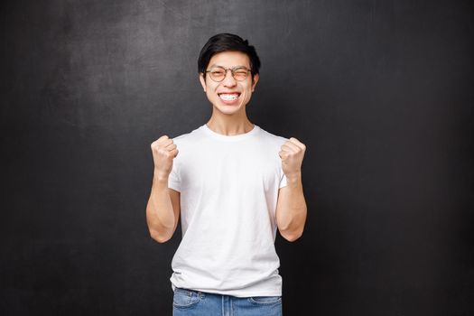 Yes I did it. Satisfied and happy asian guy passed exam, fist pump in success and celebration, wink joyfully smiling achieve goal, winning prize or reward, triumphing over victory, black background.