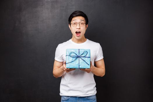 Celebration, holidays and lifestyle concept. Surprised happy young asian b-day guy receive cute wrapped present, holding gift box gasping and looking astonished, celebrating birthday.