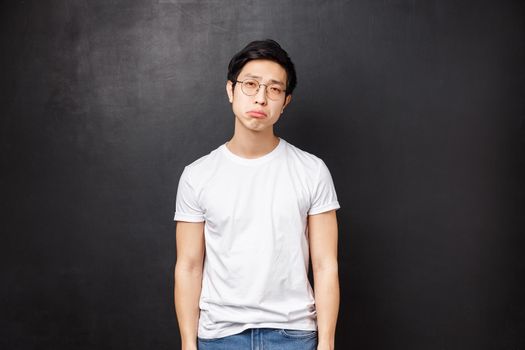 Portrait of gloomy and upset, reluctant tired young male student have lots of homework being drained with duties and part-time job, look fatigue sighing and pouting distressed, black background.