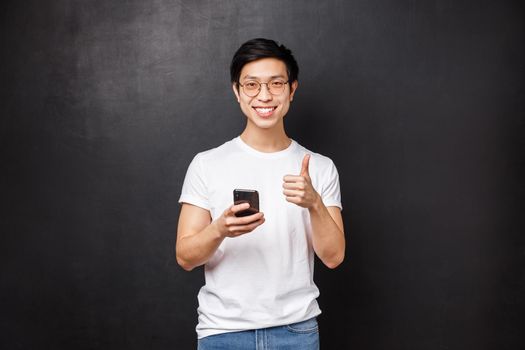 Technology, gadgets and people concept. Satisfied handsome asian guy using mobile phone application, delivery service or internet store, show thumb-up as approve and recommend app.