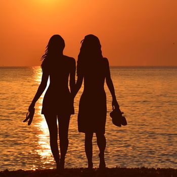 Silhouette of two lesbian girls on the beach in sunrise