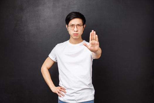 Caution do not trespass. Serious-looking confient and angry young asian guy give warning, pull arm forward in stop sign, prohibit come closer, refuse something bad, black background.