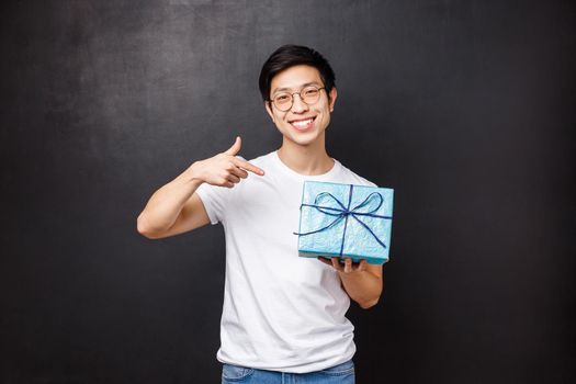 Celebration, holidays and lifestyle concept. Portrait of cheerful good-looking young asian boyfriend prepared special gift for anniversary, pointing at wrapped gift box and smiling camera.