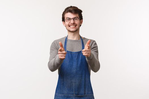 Portrait of excited handsome smiling employee in apron, coffee shop worker show thumbs-up in approval or like, barista guarantee quality of flavour and best service at store, white background.