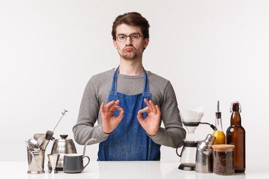 Barista, cafe worker and bartender concept. Portrait of impressed, pleased caucasian man, employee in apron and glasses make not bad sign, show okay in confirmation, approve good coffee making method.