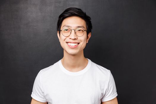 Close-up portrait of dreamy happy young asian man in white t-shirt, glasses, beaming smile excited, looking left cheerful, standing black background, remember something cute.