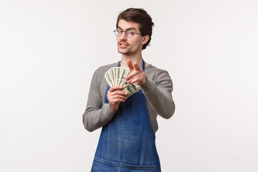 Small business, finance and career concept. Portrait of confident male entrepreneur in apron pointing at camera and holding money suggesting way how to earn cash, invite work at his coffee shop.