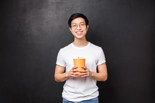 Cheerful handsome asian boyfriend bought popcorn for girlfriend while having date at cinema, smiling watching hilarious comedy, chuckle funny joke, enjoying leisure time on weekends, black background.