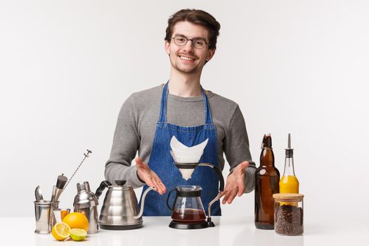 Barista, cafe worker and bartender concept. Portrait of handsome bearded male employee introduce filter coffee smiling pleased, teach how prepare perfect drink on bar counter.