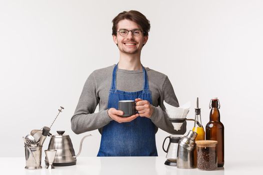 Barista, cafe worker and bartender concept. Portrait of cheerful pleasant young male employee in apron invite everyone have delicious drink, making coffee, holding tea and smiling camera.