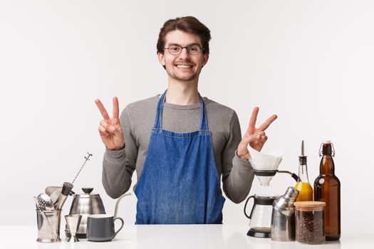 Barista, cafe worker and bartender concept. Friendly pleasant young male employee in apron, showing peace sign and smiling happy, love making coffee and make customers satisfied, prepare chemex.