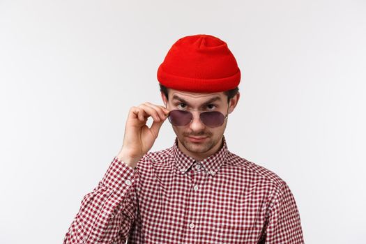 Skeptical and doubtful handsome hipster young man with moustache, red beanie, look from under forehead with disbelief, take-off glasses to make serious judgemental gaze at strange person.
