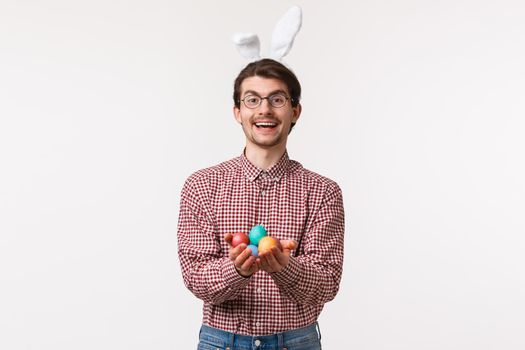 Traditions, religious holidays, celebration concept. Friendly and cheerful cute christian guy, wear rabbit ears, holding painted Easter eggs and smiling joyfully, congratulate with blessing day.
