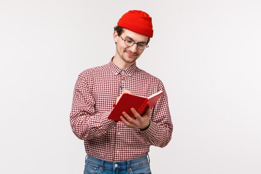 Waist-up portrait funny cute bearded guy red beanie, glasses, write down notes during lecture, making list of grocceries or have diary, smiling pleased as working on project, white background.