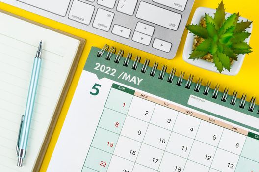 May 2022 desk calendar and diary with keyboard computer on yellow background.