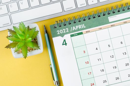 THe Arpil 2022 desk calendar and diary with keyboard computer on yellow background.