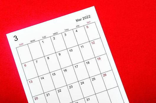 Close up March 2022 calendar sheet on red background.