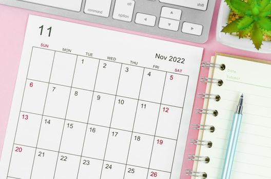 The November 2022 calendar sheet with keyboard computer on pink background.