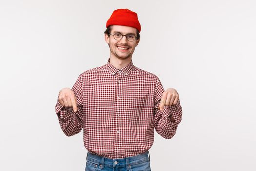 Waist-up portrait friendly-looking smiling happy and satisfied young male customer in red beanie and glasses, pointing fingers down to introduce new store or application, download banner.