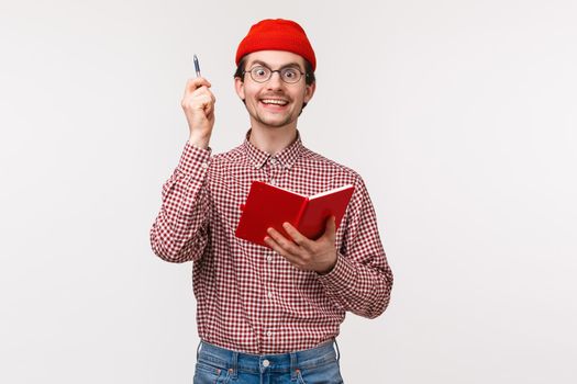 Waist-up portrait excited and thrilled young man striked with awesome idea, say eureka and lift pen up with satisfied inspired smile, holding notebook, solving difficult equation, white background.