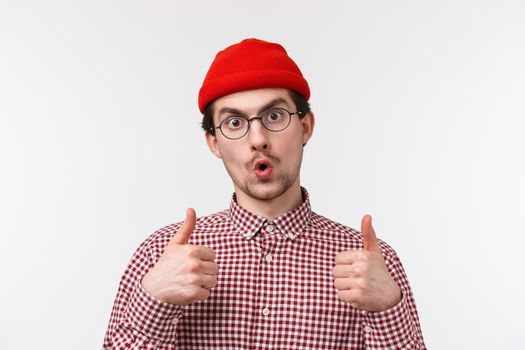 Emotions and people concept. Close-up portrait impressed funny bearded caucasian man in beanie and checked shirt, wear glasses, show thumbs-up satisfied, rate good product, like and approve.