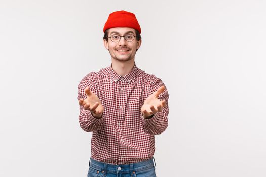 Waist-up portrait pleasant funny young man with beard in red beanie, holding hands as if ready to receive something, get present, catching object, standing white background.
