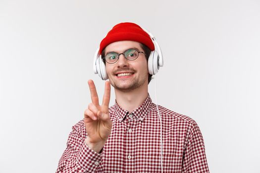 Music, technology and people concept. Peace dudes. Cheerful cute hipster man in glasses and check shirt, wear glasses listening music in headphones stay positive, smile and show goodwill sign.